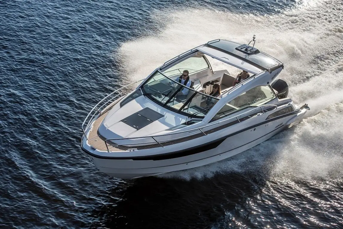 Luxury motorboat cruising on water, with two people visible in the cockpit, leaving a wake behind.